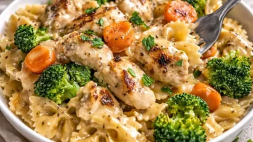 Cremige Cheddar- und Havarti-Hähnchen-Bowtie-Pasta mit geröstetem Gemüse auf einem Teller