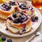 Blaubeer-Käsekuchen-Wirbelbrötchen auf einem Teller, garniert mit frischen Heidelbeeren.