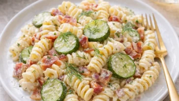 Dillgurken-Bacon-Pasta-Salat auf einem Teller garniert mit frischen Kräutern
