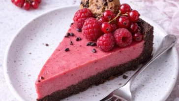 Himbeermousse-Schoko-Cookie-Tarte auf einem Teller serviert, dekoriert mit frischen Himbeeren.