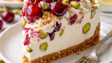 Kirschen-Pistazien-Käsekuchen auf einem Teller mit frischen Kirschen.