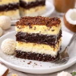 Kokos-Creme-Kuchen mit RAFFAELLO auf einem Teller, dekoriert mit Kokosraspeln