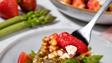 Grüner Spargel Erdbeer Salat mit karamellisierten Nüssen serviert auf einem Teller