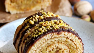 Pistazien-Marzipan-Roulade auf einem Teller mit frischen Pistazien.