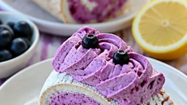 Roulade Pavlova mit Johannisbeeren und Kokos auf einem Teller serviert.