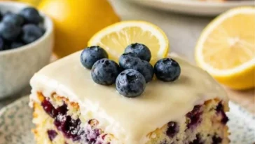 Zitronen-Blaubeer-Kuchen mit cremigem Cheesecake-Guss auf einem weißen Teller