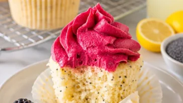 Fluffige Zitronen-Mohn-Cupcakes mit aromatischem Brombeer-Überzug auf einem Teller.