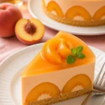 Pfirsich-Mousse-Kuchen auf einem Teller, dekoriert mit frischen Pfirsichen.