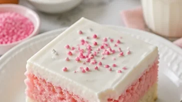 Rosa Vanillekuchenwürfel auf einem Teller, dekoriert mit Sahne