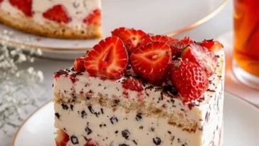 Erdbeer-Stracciatella-Torte auf einem Teller mit frischen Erdbeeren und Schokoladensplittern