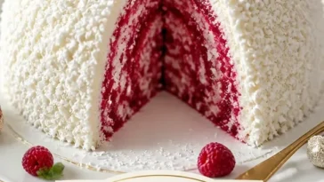 Fluffige Kokos-Schneeball-Torte mit Himbeerwirbel auf einem Teller angerichtet.